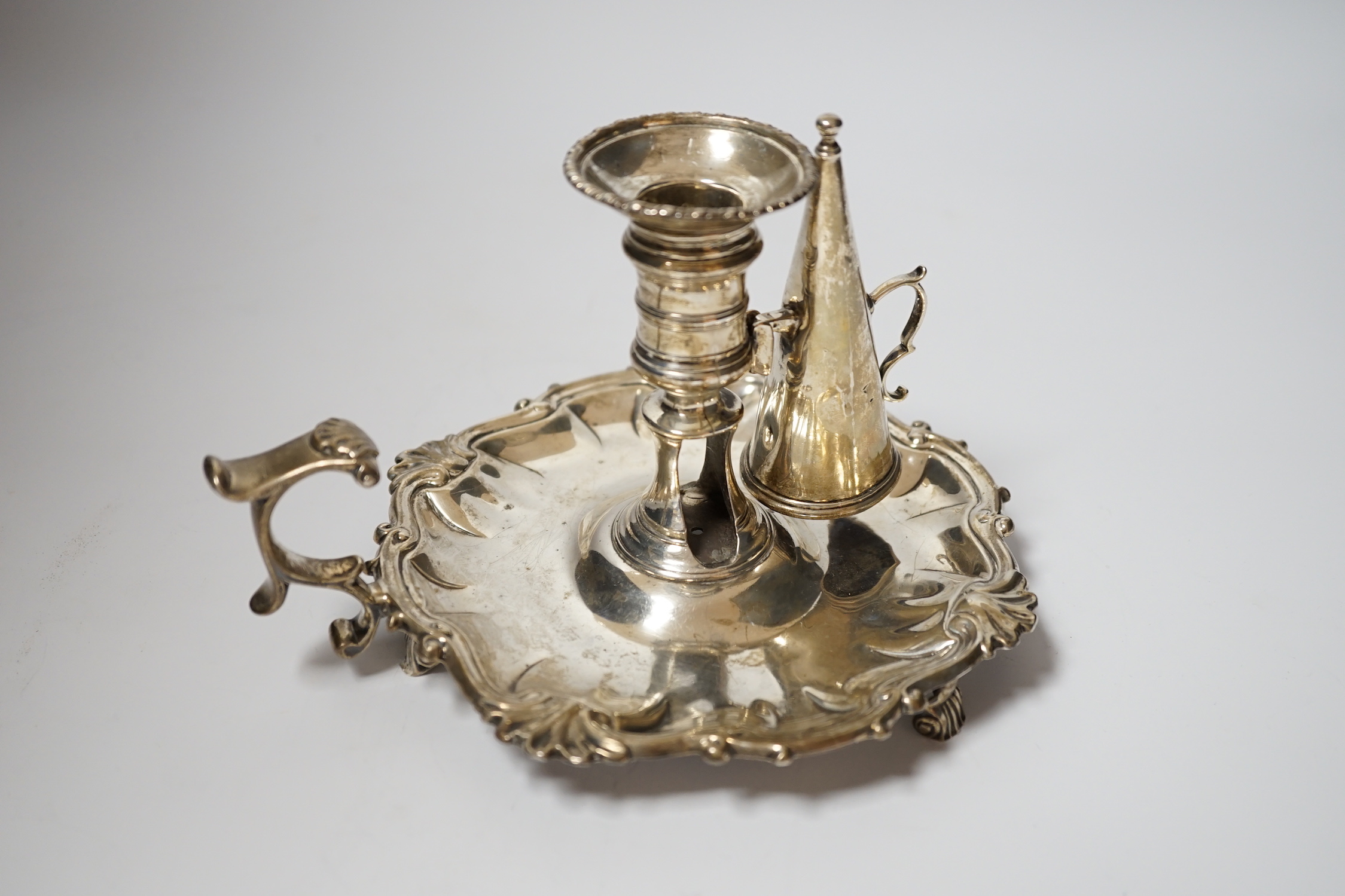 A George II silver chamberstick, with shell border, on three scroll feet, William Grundy, London, 1756, with extinguisher(marks rubbed), overall 18.5cm, 14.1oz.